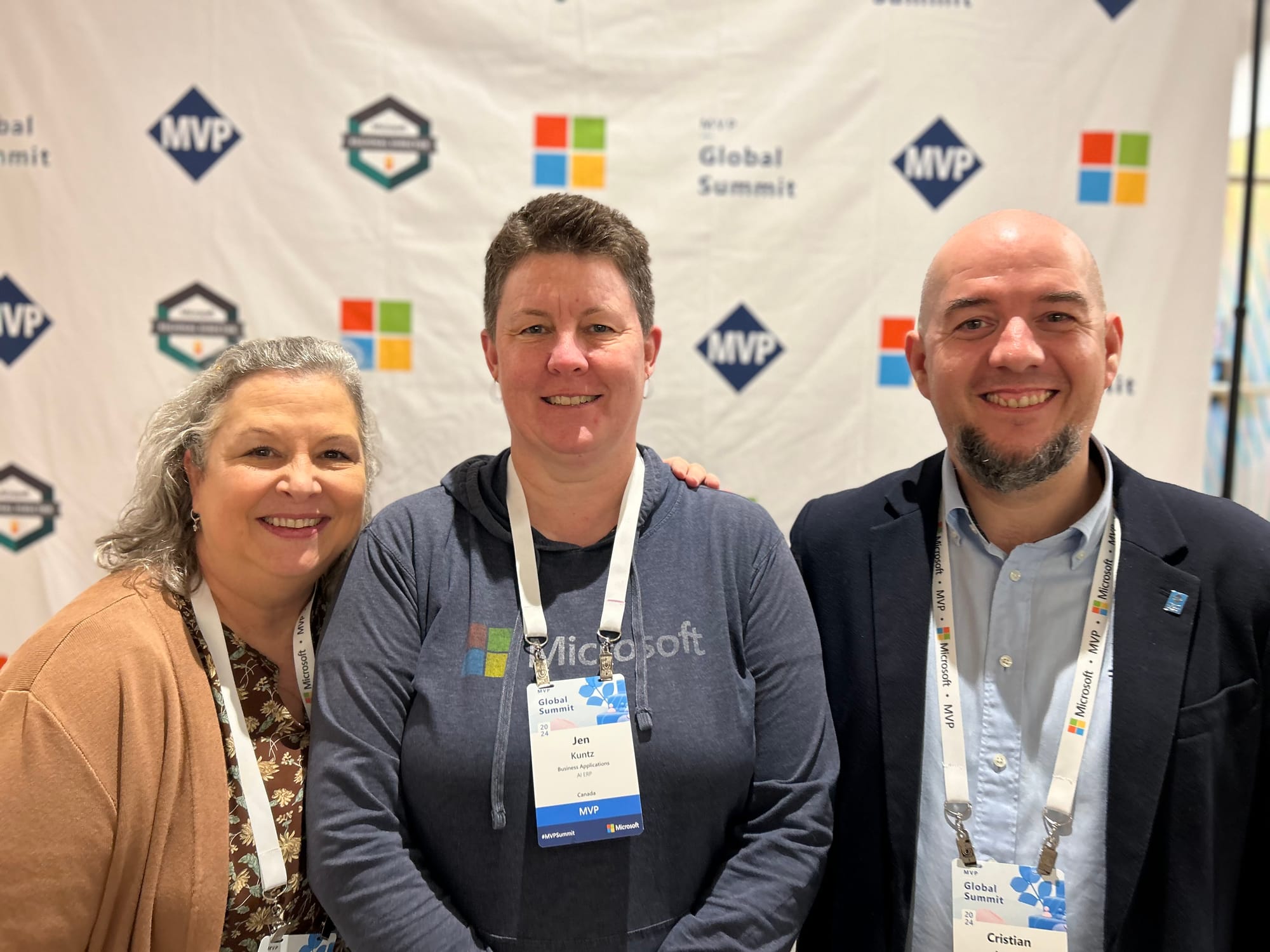 Belinda Allen, a smiling woman with long grey hair, wearing a light brown sweater over a dark brown floral shirt; Jen/me, with short brown hair, wearing a blue long sleeve hooded shirt with the Microsoft logo on the front and a lanyard around my neck; Cristian Angyal, with a shaved head and black goatee, wearing a light blue button down shirt underneath a dark blue blazer, with a lanyard around his neck.