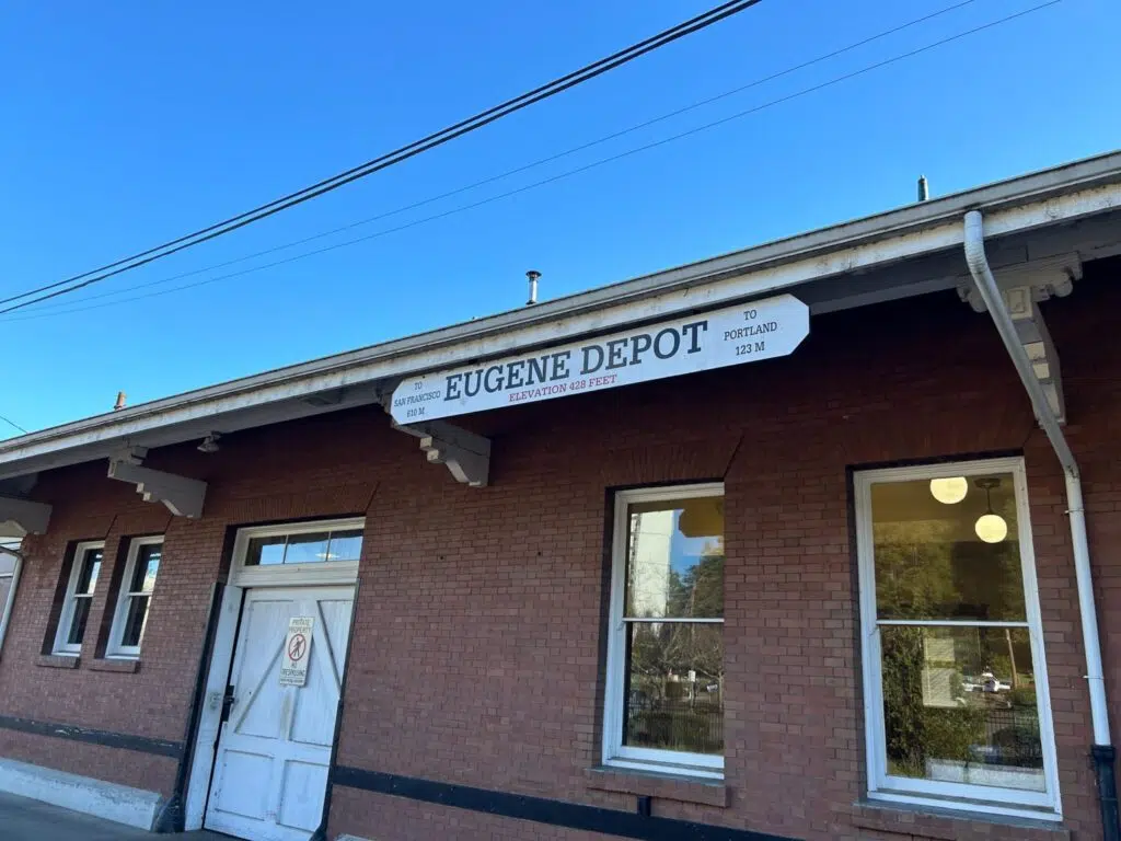 Historic brick Eugene Depot train station building with directional sign showing distances to San Francisco and Portland.