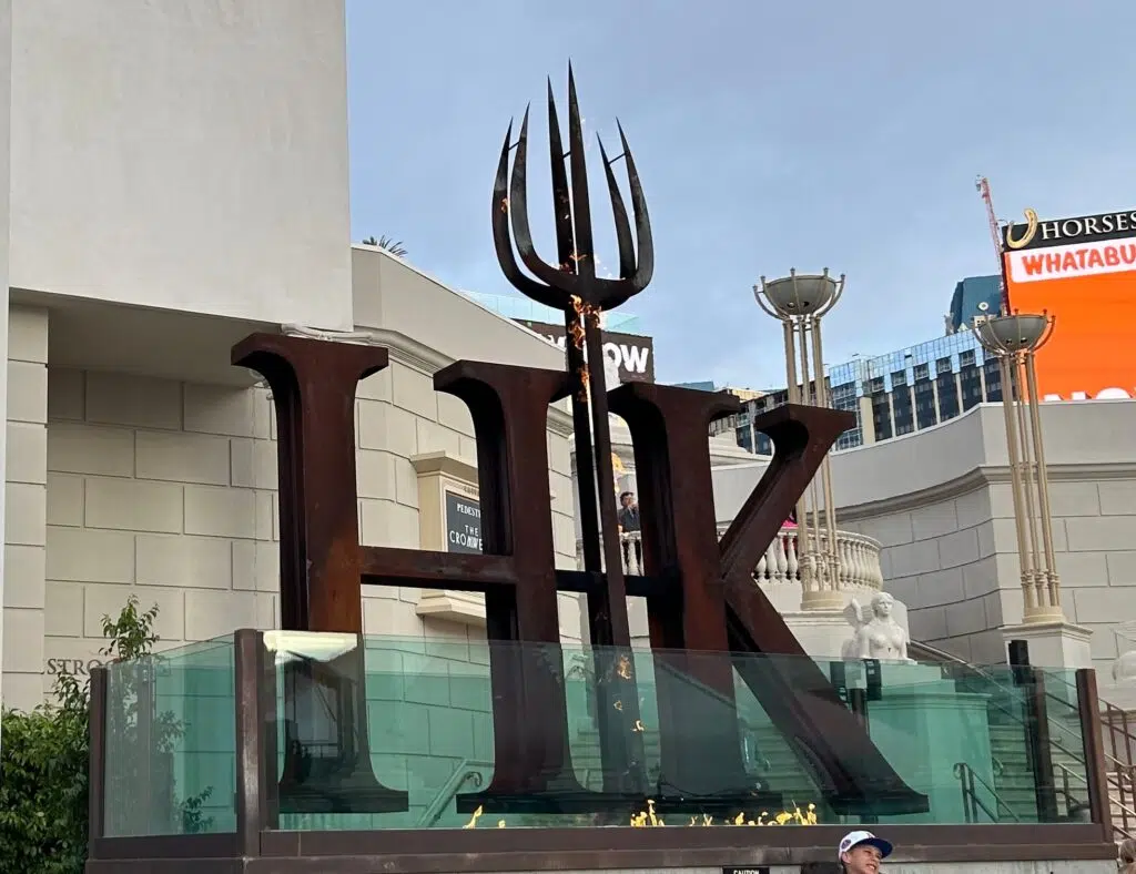 Large HK letters with pitchfork sculpture at Hell's Kitchen restaurant entrance in Las Vegas, with flames at the base.