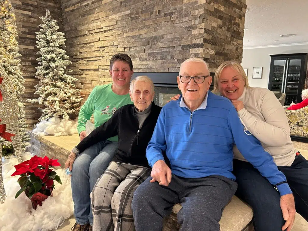 Myself and the Munro family smiling together in a room decorated for Christmas with a poinsettia, Christmas tree, and stone fireplace.