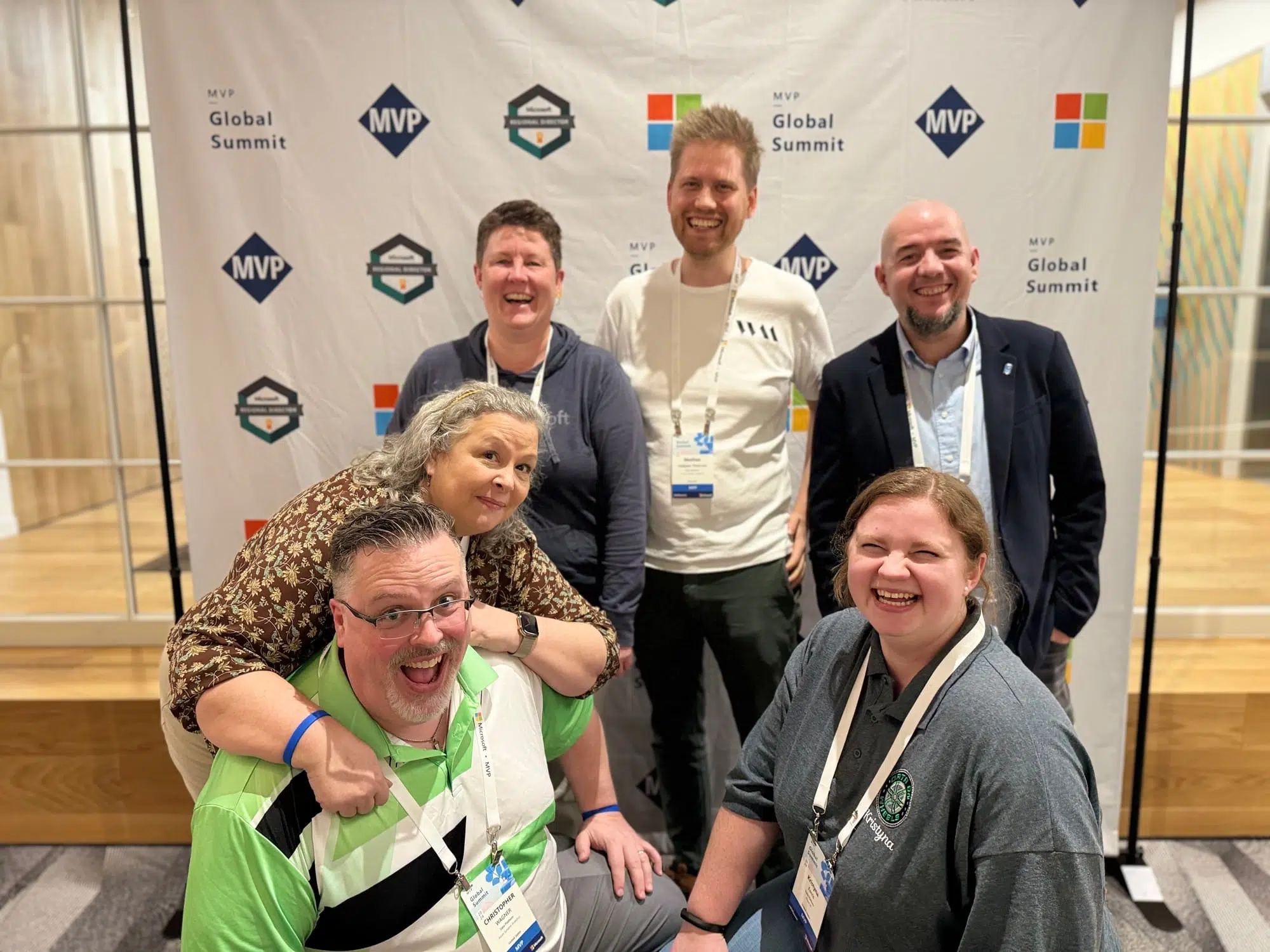 A group of people laughing while posing for the picture. From front left to right: Chris Wagner in a green, black and white t-shirt and eyeglasses, partially kneeling on the floor; Belinda Allen with long grey hair, leaning with her arms around Chris’ shoulders, wearing a brown floral shirt; me with a blue hooded shirt and short brown hair; Mathias Halkjaer in a white t-shirt and a lanyard around his neck, with blond spiky hair and brown facial hair; Cristian Angyal with a shaved head and black goatee, wearing a light blue button down shirt and dark blue blazer; Kristyna Ferris with long brown hair tied back in a ponytail, kneeling in front right in front of Cristian with a grey golf shirt and a lanyard around her neck.
