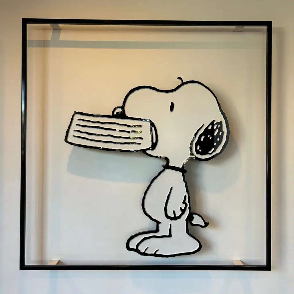 Framed wall art of Snoopy from Peanuts comic strip holding his dog dish in his mouth.