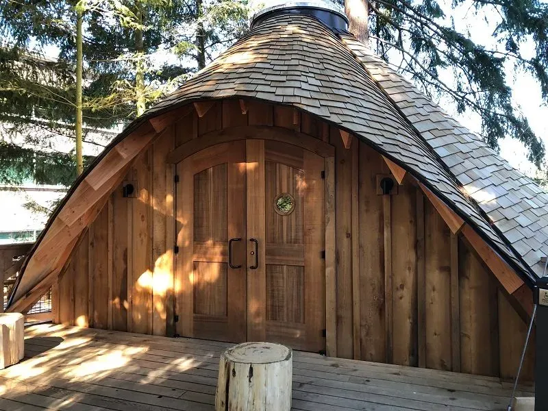 Wooden treehouse with conical shingled roof, arched doorway with circular window, and wooden deck at Microsoft Redmond campus