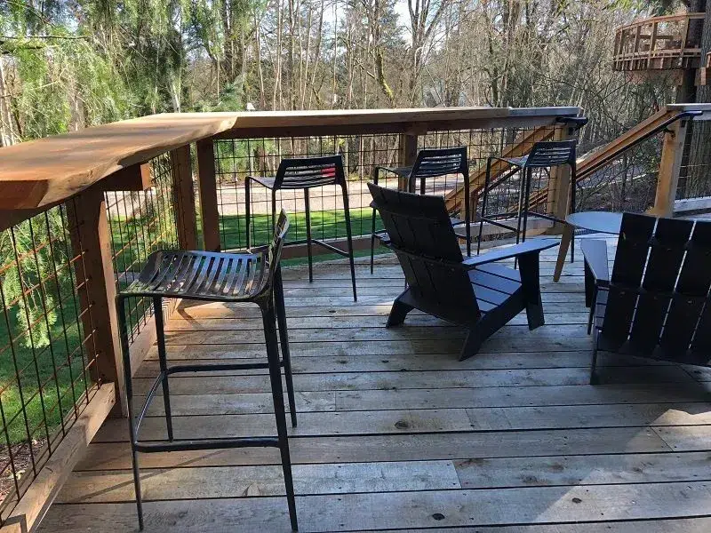 Outdoor deck seating area at Microsoft Treehouses in Redmond, featuring bar stools, Adirondack chairs, and forest views