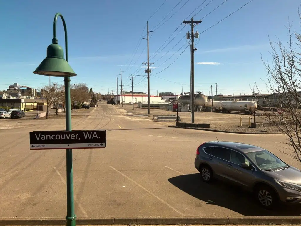 Vancouver, WA Amtrak station sign with directional arrows pointing to Seattle and Portland, parking lot and railyard visible.